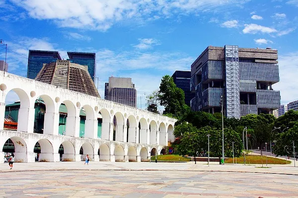 a white archway with many arches in front of a building with trees and buildings in the background