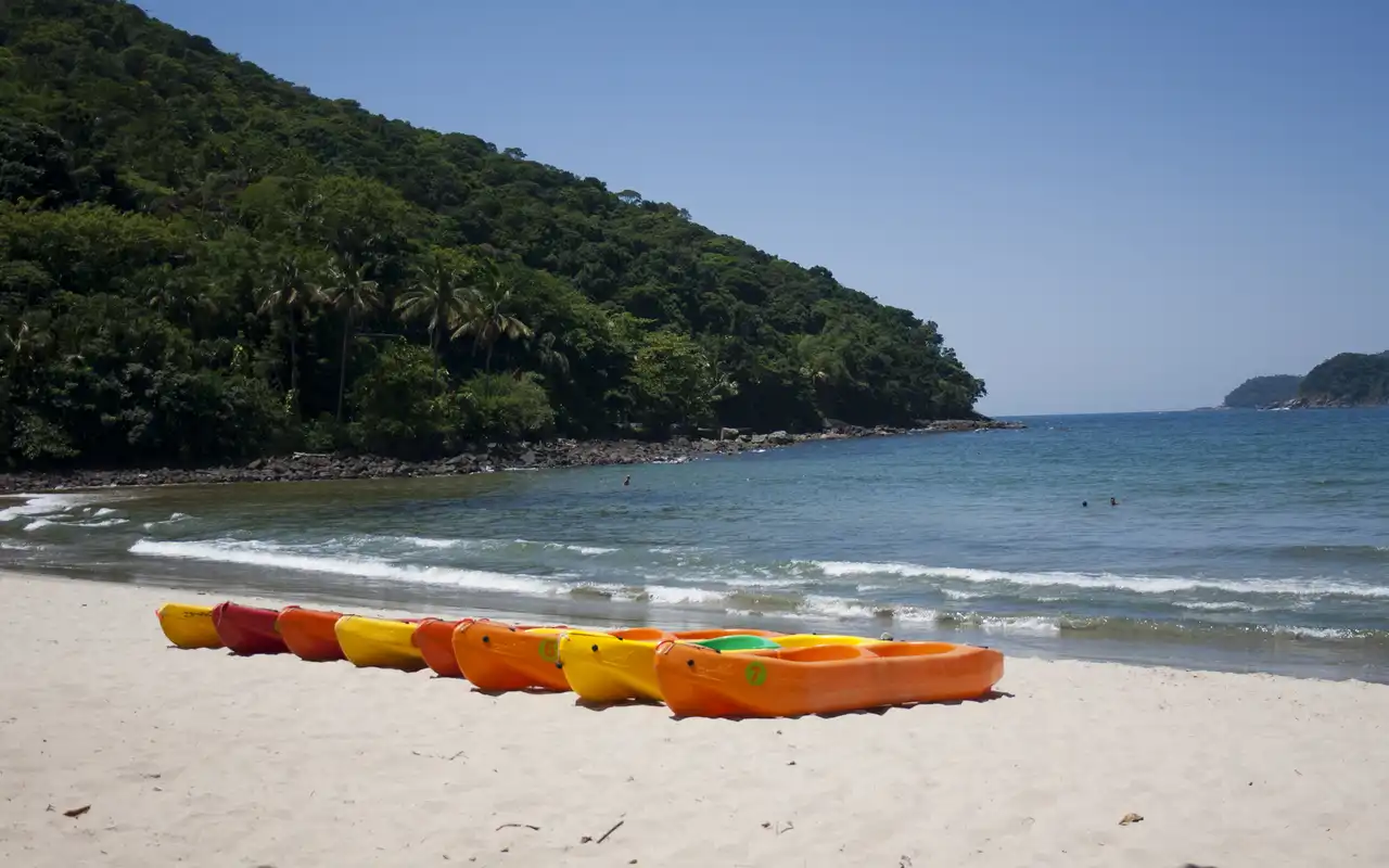 Vista panorâmica da Praia da Barra do Sahy em São Sebastião, SP. Mar calmo e esverdeado, em formato de ferradura, cercado por Mata Atlântica e costões rochosos.