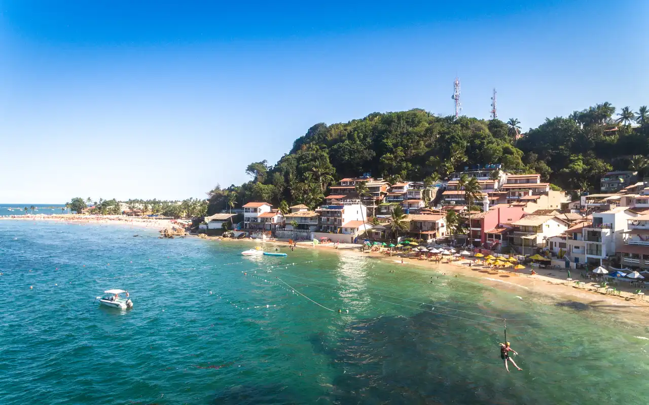 Turistas descendo a tirolesa em direção às águas claras da Primeira Praia em Morro de São Paulo