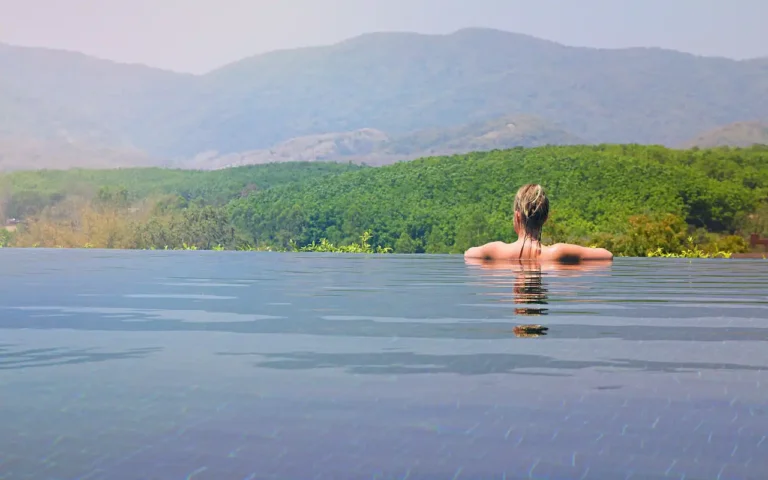 Pessoa relaxando em uma piscina de borda infinita com vista para as montanhas; realize a viagem dos sonhos economizando na hospedagem com o cupom Booking 2026